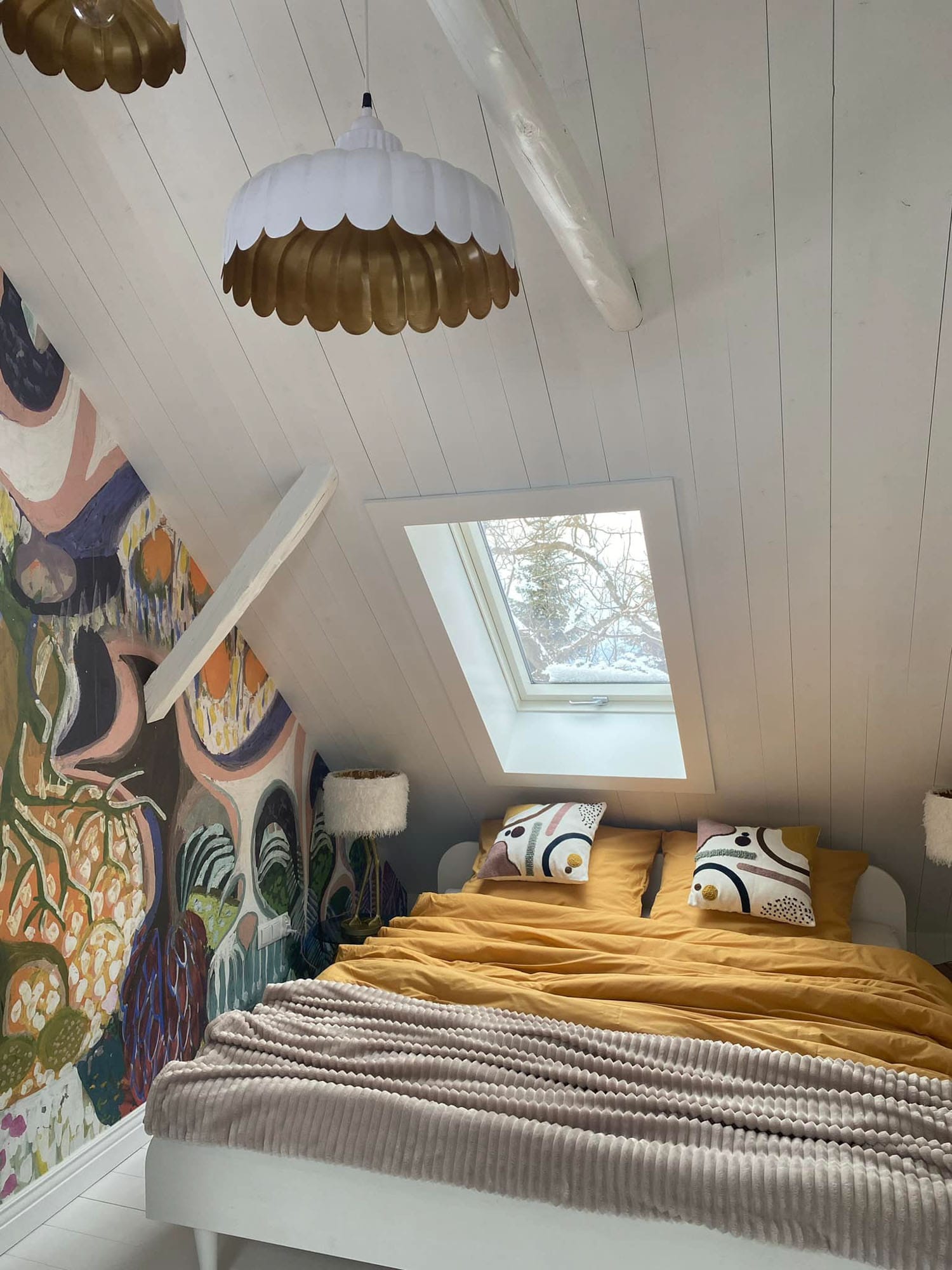 An attic bedroom in a mountain cabin featuring 'Purchawkowy Las' wallpaper by FREZO. The colorful, forest-inspired mural creates a cozy and artistic retreat in the Beskid mountains.
