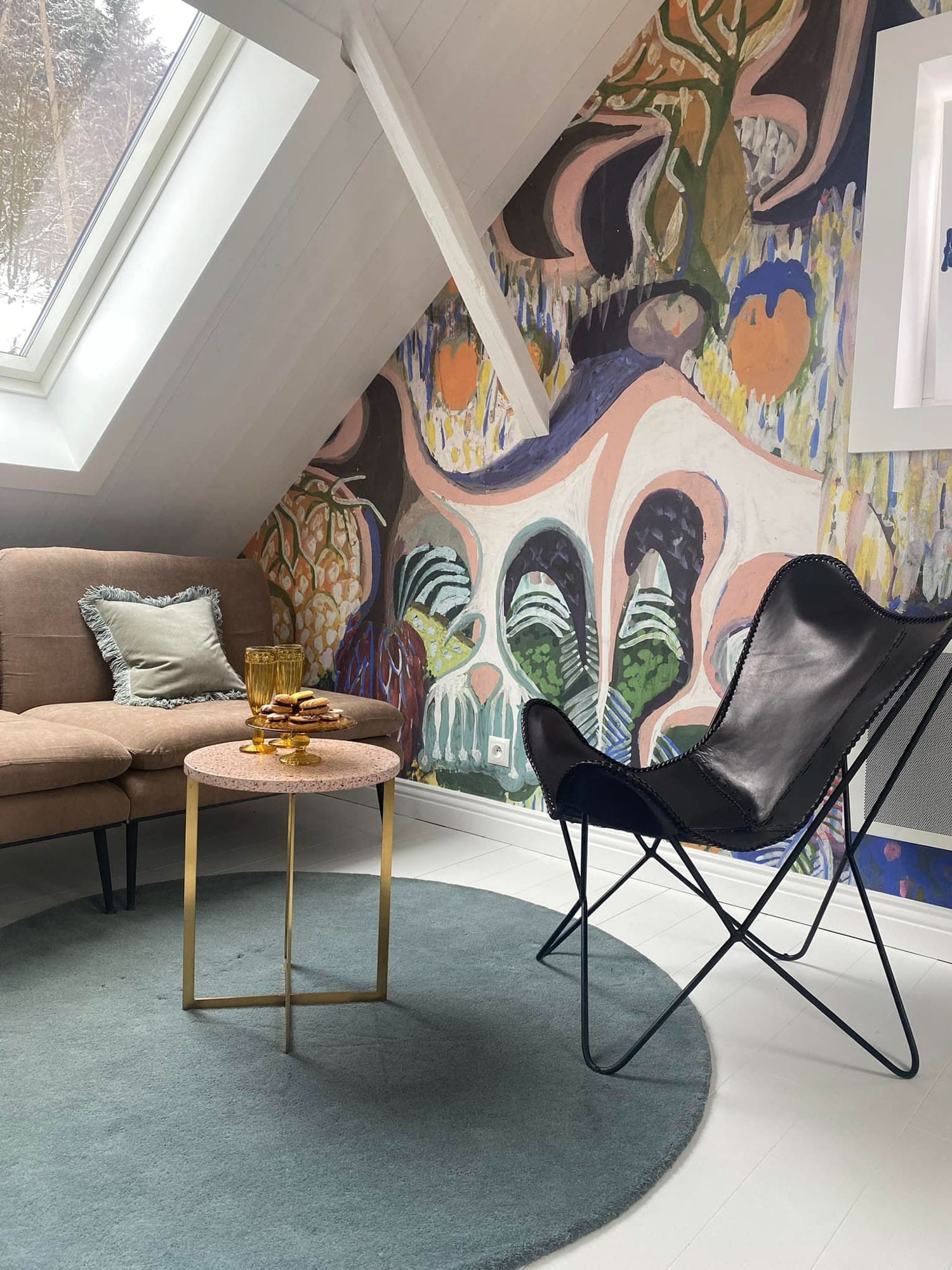 An attic bedroom in a mountain cabin featuring 'Purchawkowy Las' wallpaper by FREZO. The colorful, forest-inspired mural creates a cozy and artistic retreat in the Beskid mountains.